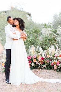 a bride and groom embrace in front of a flower garden